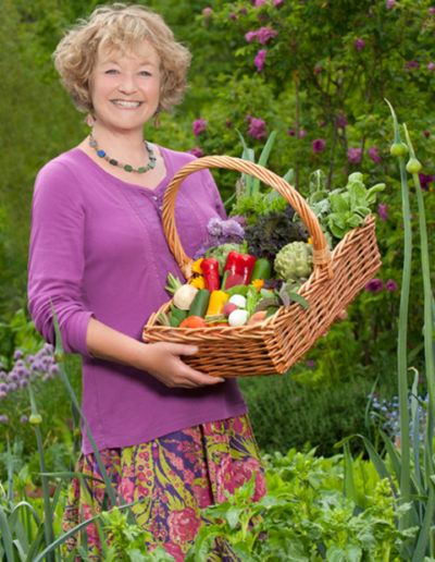 On location portrait of author in her farm garden holding produce.
