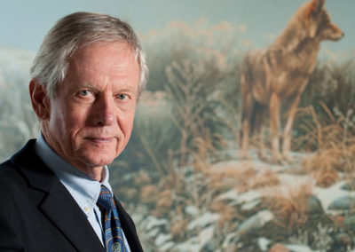 Robert Bateman poses with painting of a wolf in the background at on location photo shoot