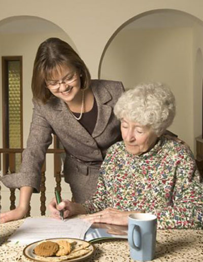 Older woman signs document with the help of others in posed on location portrait