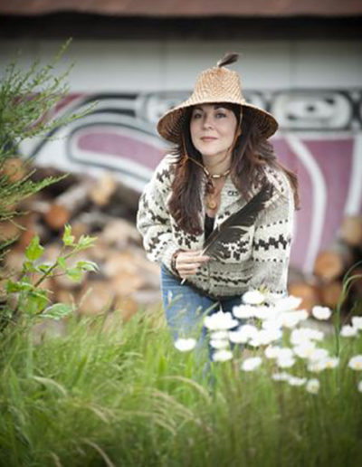 Aboriginal native artist poses for outdoor portrait beside decorated longhouse