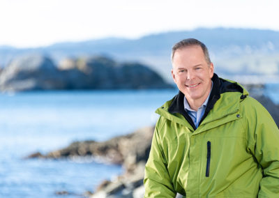 Headshot of man standing by the ocean in green jacket